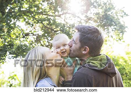 Picture - Caucasian couple kissing baby in backyard. Fotosearch