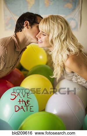 Stock Photograph - Caucasian couple kissing over balloon with 'save the date text. Fotosearch
