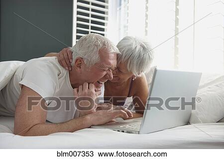 Caucasian couple laying in bed and using laptop View Large Photo Image Stock Image - Caucasian couple laying in bed and using laptop. Fotosearch