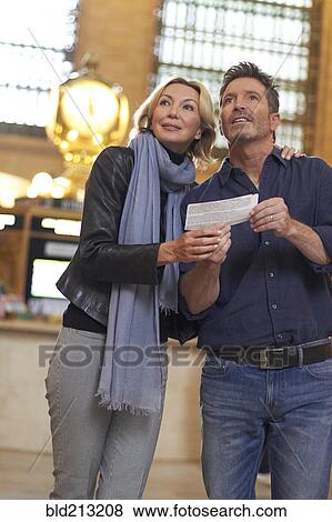 Stock Photo - Caucasian couple reading train schedule in Grand Central Station, New York City, New York, United States. Fotosearch