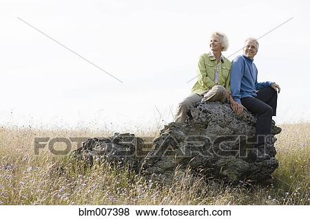 Stock Photo - Caucasian couple sitting on rock in field. Fotosearch
