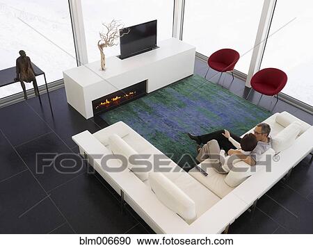Stock Image - Caucasian couple sitting on sofa in modern living room. Fotosearch