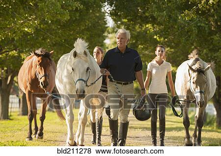 Stock Photo - Caucasian family walking horses on dirt path. Fotosearch