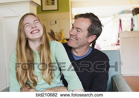 Stock Image - Caucasian father and daughter laughing in living room. Fotosearch