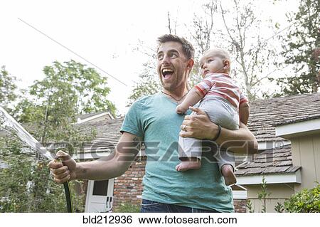 Stock Photograph - Caucasian father holding baby and watering plants. Fotosearch