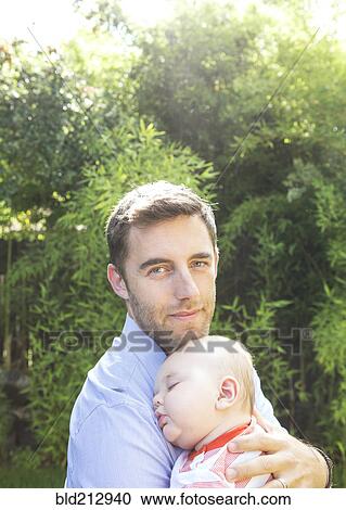 Stock Image - Caucasian father holding baby in backyard. Fotosearch