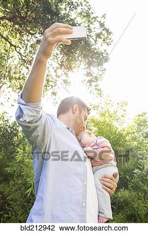 Caucasian father taking cell phone picture with baby in backyard View Large Photo Image Stock Image - Caucasian father taking cell phone picture with baby in backyard. Fotosearch