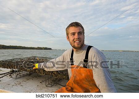 Stock Image - Caucasian fisherman holding net on boat. Fotosearch