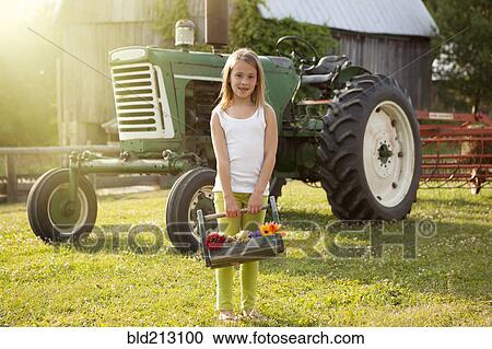 Stock Image - Caucasian girl holding basket of flowers on farm. Fotosearch