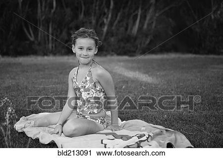 Stock Image - Caucasian girl sitting on towel in backyard. Fotosearch
