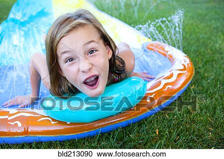 Stock Image - Caucasian girl smiling on water slide. Fotosearch