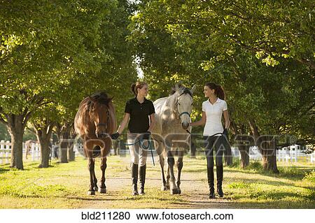 Stock Image - Caucasian girls walking horses on dirt path. Fotosearch
