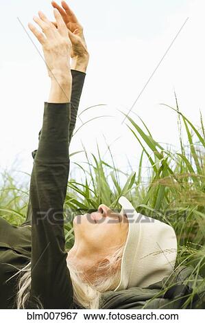 Stock Photo - Caucasian laying in grass with arms raised. Fotosearch