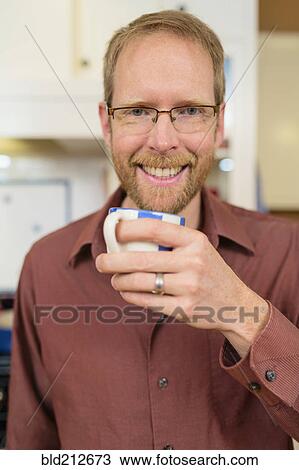 Stock Image - Caucasian man drinking cup of coffee in kitchen. Fotosearch