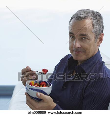 Stock Photo - Caucasian man eating fruit salad. Fotosearch