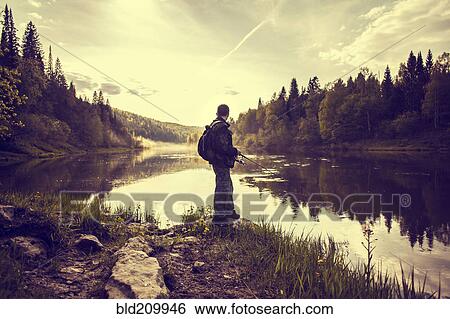 Stock Photograph - Caucasian man fishing at lakeside. Fotosearch