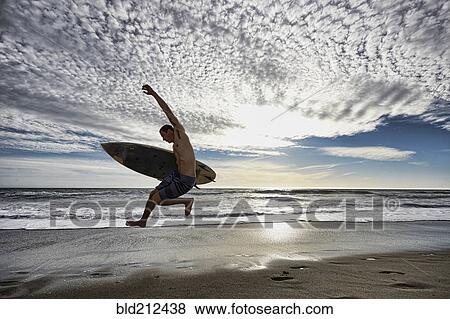 Caucasian man jumping with surfboard on beach View Large Photo Image Stock Photo - Caucasian man jumping with surfboard on beach. Fotosearch