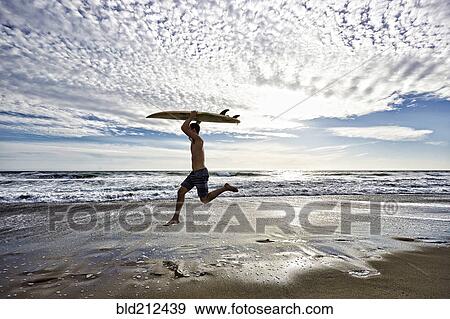 Caucasian man jumping with surfboard on beach View Large Photo Image Stock Photo - Caucasian man jumping with surfboard on beach. Fotosearch