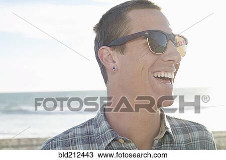 Stock Image - Caucasian man laughing on beach. Fotosearch