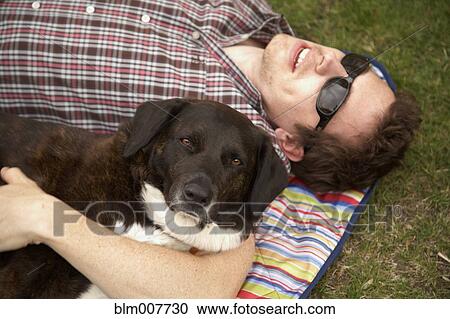 Stock Image - Caucasian man laying in park with dog. Fotosearch