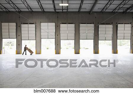 Stock Photo - Caucasian man moving boxes in empty warehouse. Fotosearch
