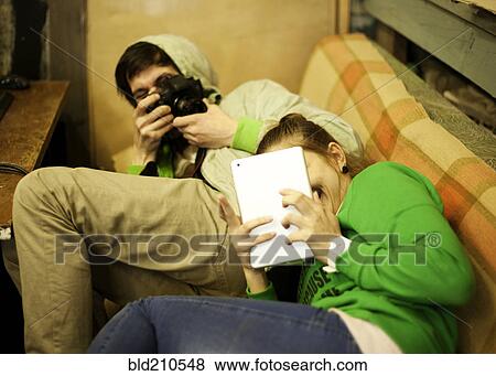 Stock Photo - Caucasian man photographing girlfriend on sofa. Fotosearch