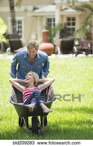 Stock Image - Caucasian man pushing girlfriend in wheelbarrow. Fotosearch