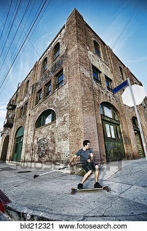 Stock Image - Caucasian man riding skateboard with land paddle. Fotosearch