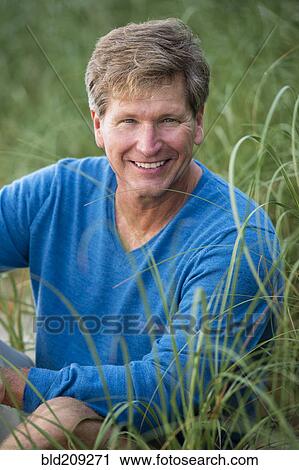 Stock Image - Caucasian man sitting in tall grass. Fotosearch