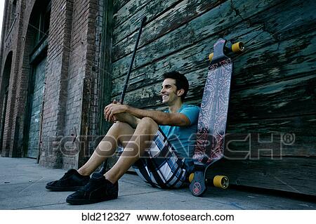 Stock Photo - Caucasian man sitting with skateboard and land paddle. Fotosearch