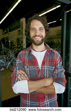 Stock Image - Caucasian man smiling in bicycle shop. Fotosearch
