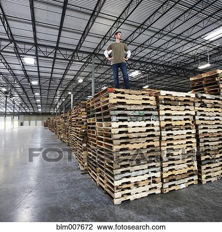 Stock Image - Caucasian man standing on wooden pallets in warehouse. Fotosearch