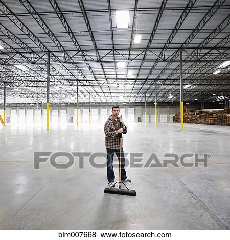 Stock Photo - Caucasian man sweeping large, empty warehouse. Fotosearch