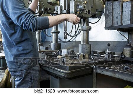 Stock Photo - Caucasian man using drilling machine in workshop. Fotosearch