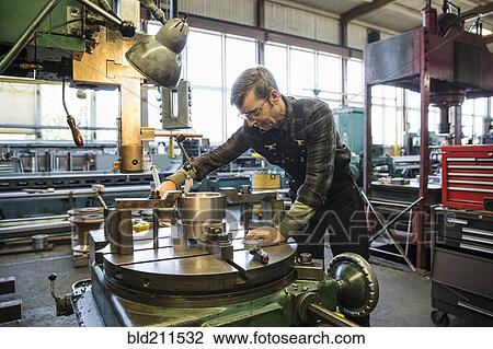 Stock Image - Caucasian man using machinery in metal shop. Fotosearch
