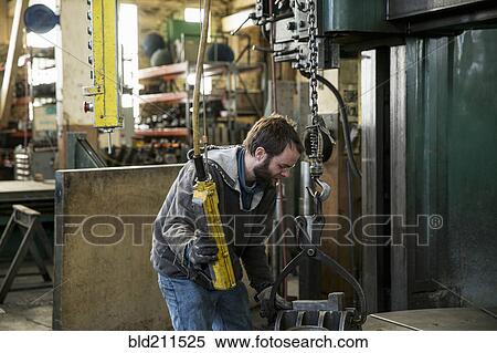 Stock Photography - Caucasian man using machinery in metal shop. Fotosearch