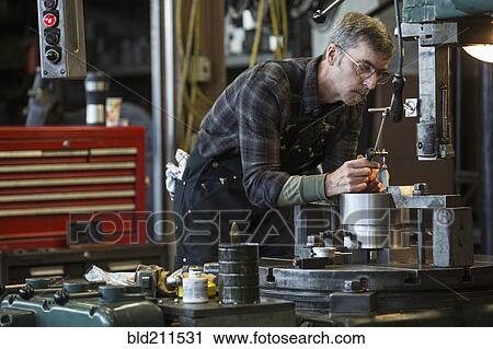 Stock Image - Caucasian man using machinery in workshop. Fotosearch