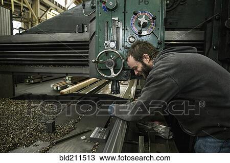 Stock Image - Caucasian man working at machinery in metal shop. Fotosearch