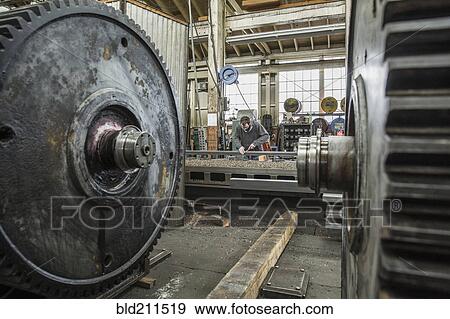 Stock Photo - Caucasian man working behind metal cogs in metal shop. Fotosearch