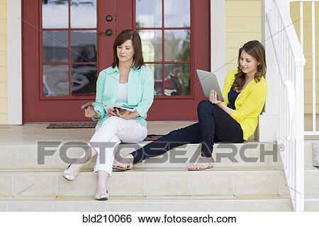 Stock Photograph - Caucasian mother and daughter relaxing on front steps. Fotosearch