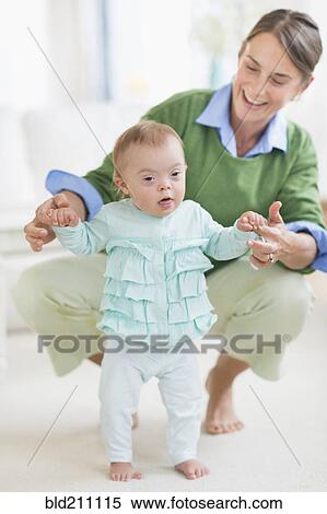 Stock Photography - Caucasian mother helping baby with Down Syndrome walk. Fotosearch