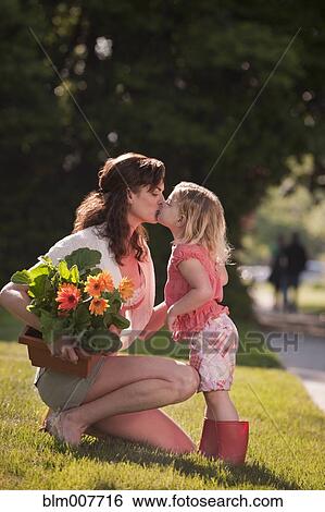 Stock Photograph - Caucasian mother holding flowers and kissing daughter. Fotosearch