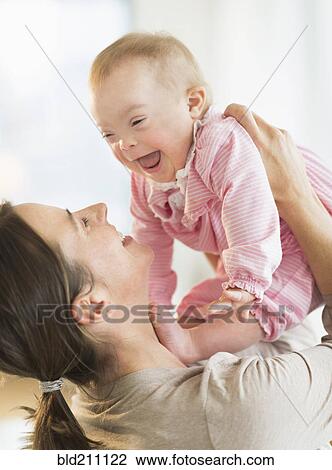 Stock Image - Caucasian mother playing with baby girl with Down Syndrome. Fotosearch