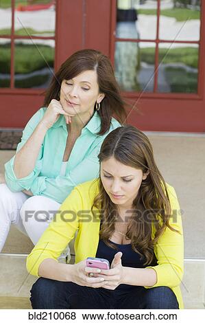 Stock Photo - Caucasian mother watching daughter use cell phone. Fotosearch