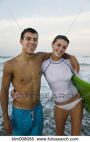 Stock Photography - Caucasian teenage couple with surfboard hugging and smiling. Fotosearch