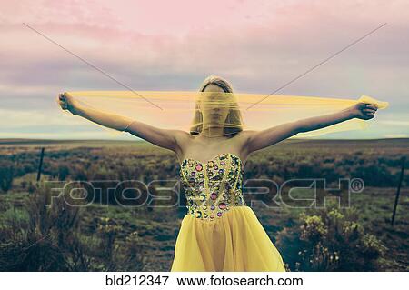 Stock Photo - Caucasian teenage girl playing with scarf in rural field. Fotosearch