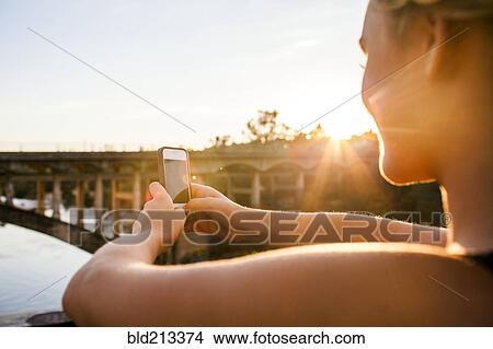 Picture - Caucasian teenage girl taking cell phone photograph of bridge. Fotosearch