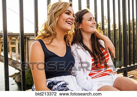 Stock Image - Caucasian teenage girls relaxing on bridge. Fotosearch