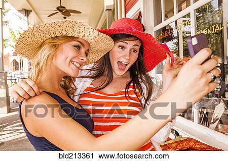Stock Image - Caucasian teenage girls taking cell phone selfie in hats. Fotosearch