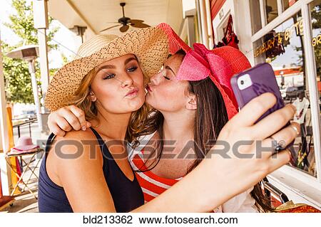 Stock Image - Caucasian teenage girls taking cell phone selfie in hats. Fotosearch